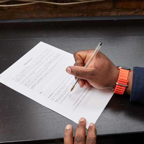 Black person writing answers to questions on a piece of paper. Focus on hand.