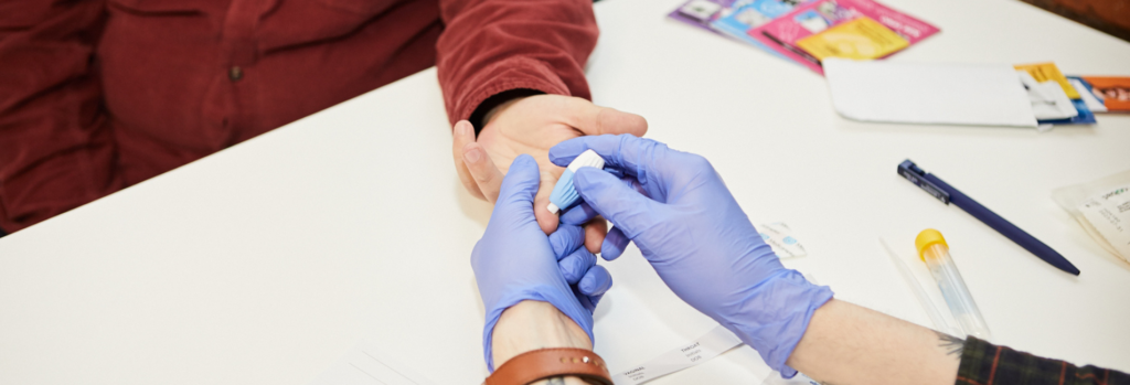 A person being pricked in the finger as part of a sexual health test.