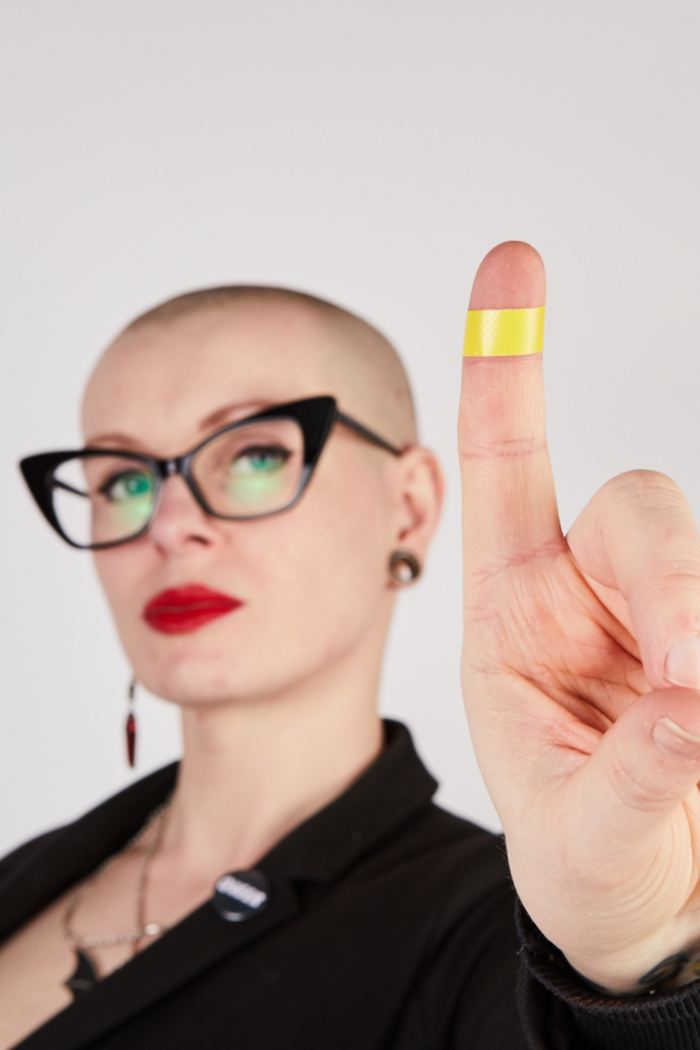 Fem-presenting person showing finger to camera confidently. Focus on bright yellow plaster on finger.