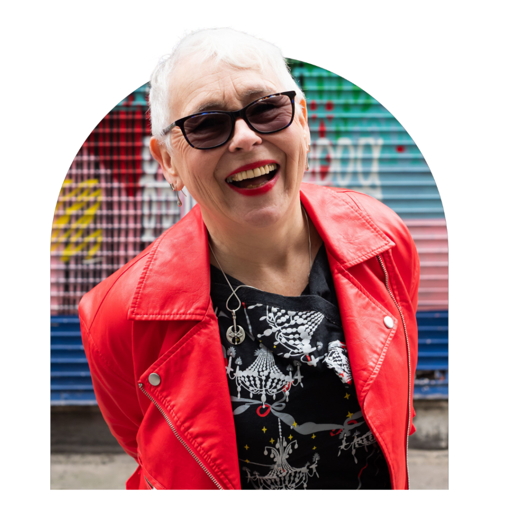 Older woman in red leather jacket with sunglasses leaning towards and smiling brightly at camera. Portrait.