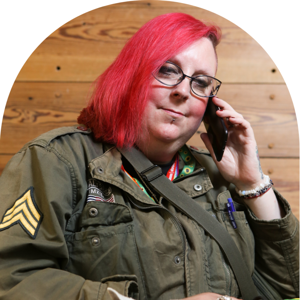 A fem-representing person in red hair on phone, looking calm.