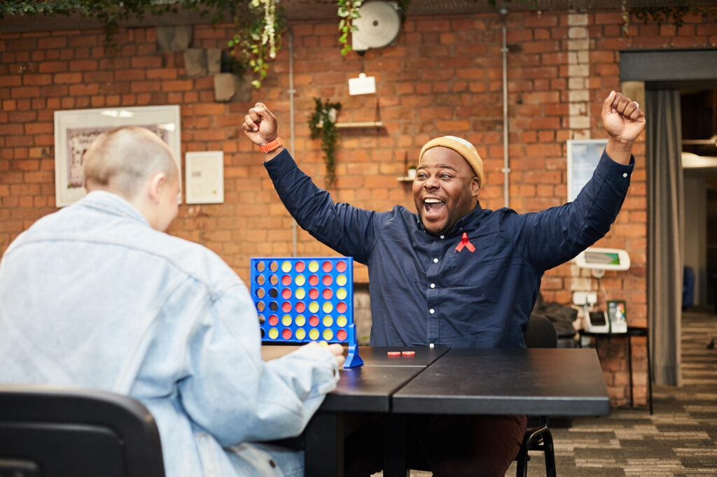 Two people playing board game. The black man facing camera cheering with both arms in the air.