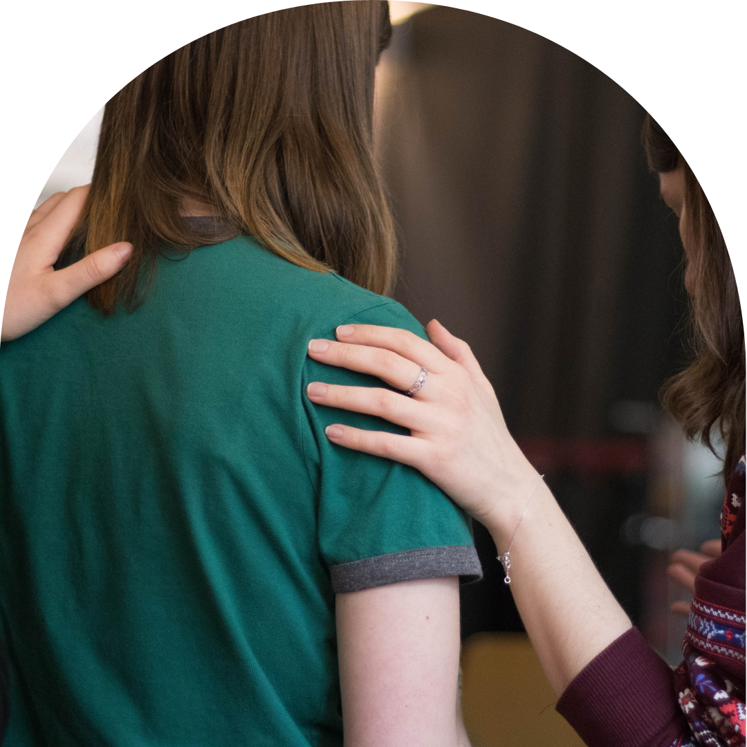 Two people outside camera frame holding shoulder of woman in green t-shirt, trying to comfort.