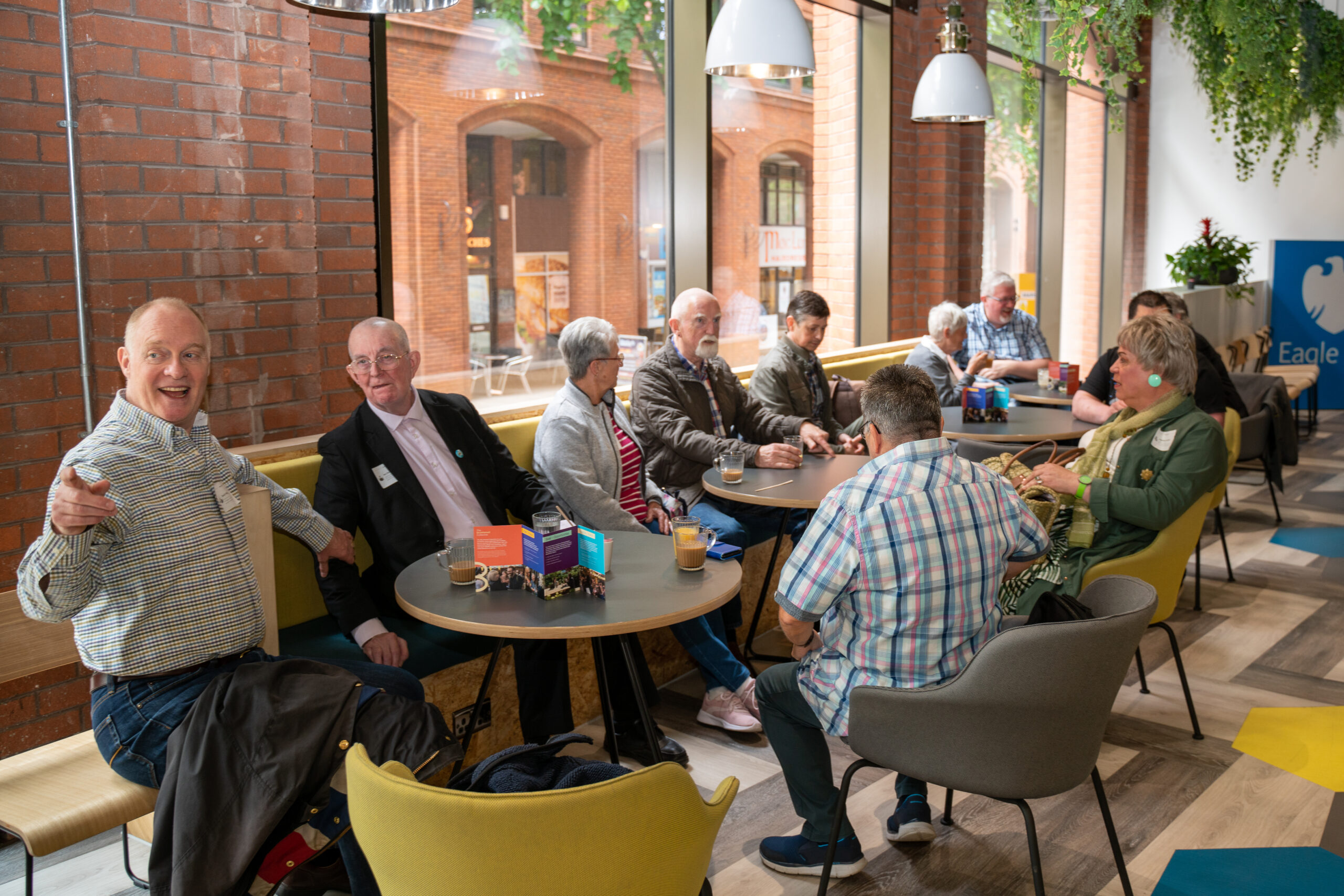 A wide shot of a group of older LGBTQ+ people in a café socialising