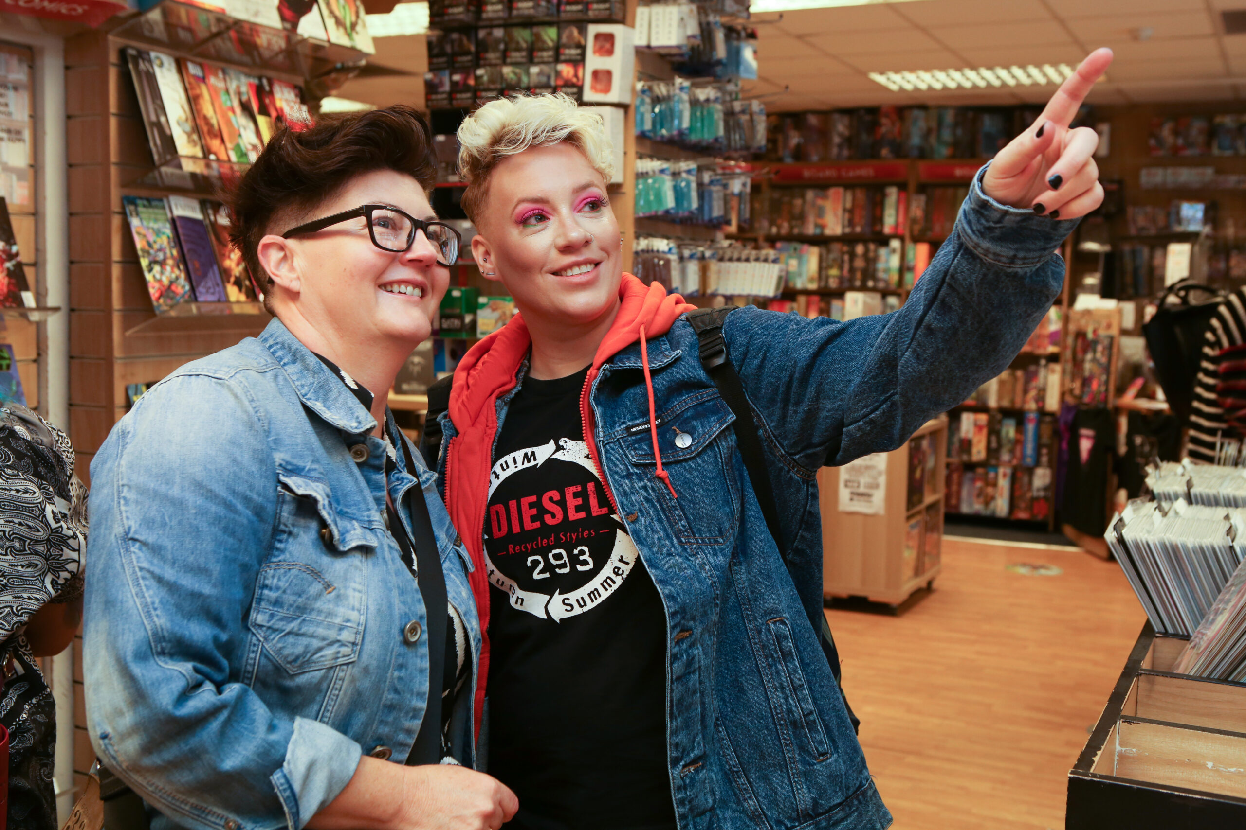 Two LGBTQ+ individuals in a bookshop looking and pointing at a piece of artwork.