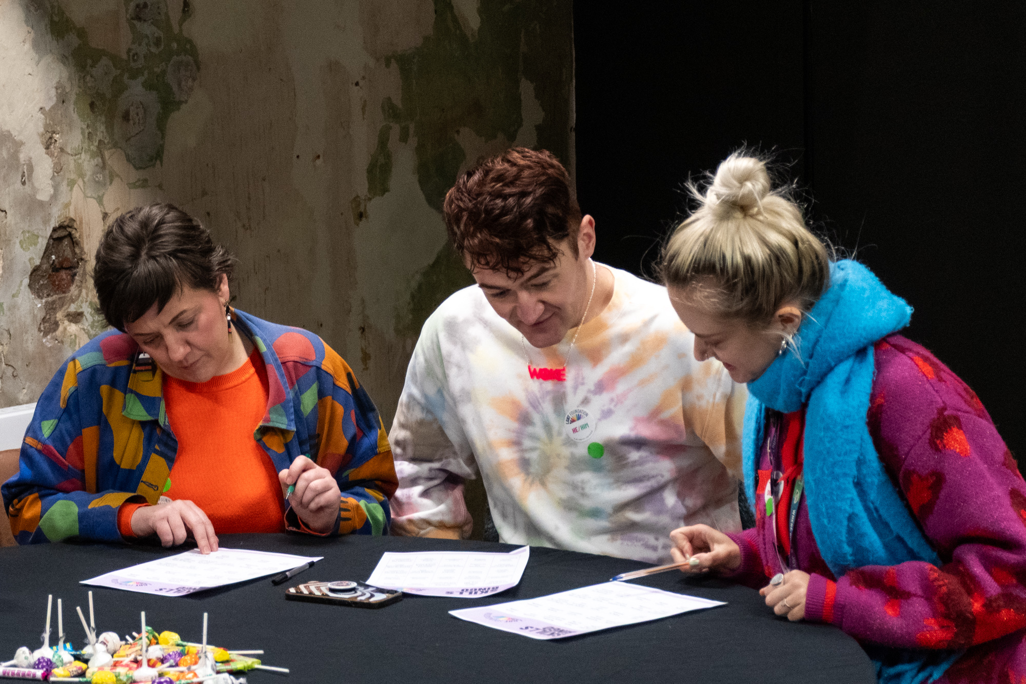 Three people around a circular table looking at a quiz sheet and working together.