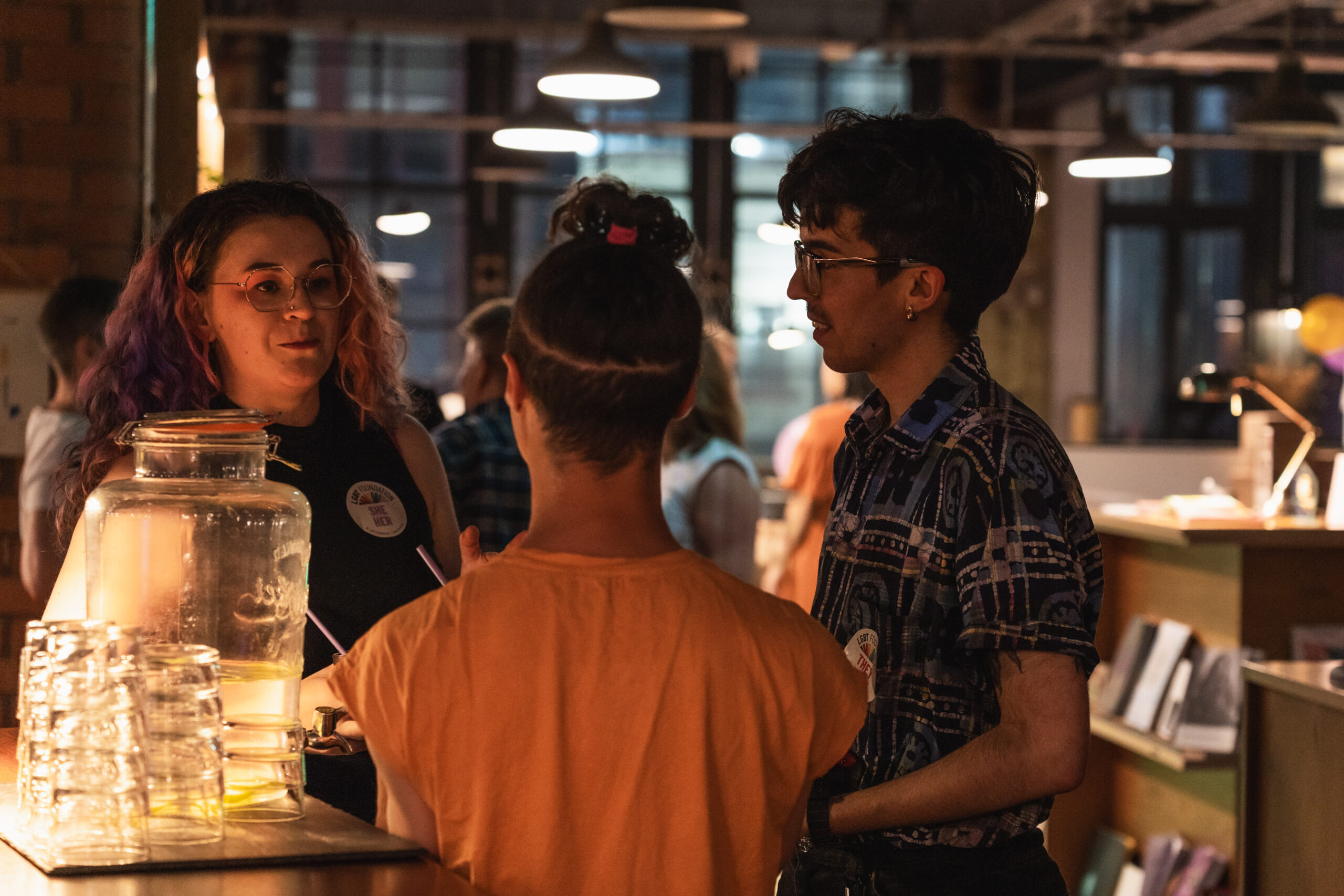 A group of three people chatting and smiling in a low-lit event space (SEESAW).
