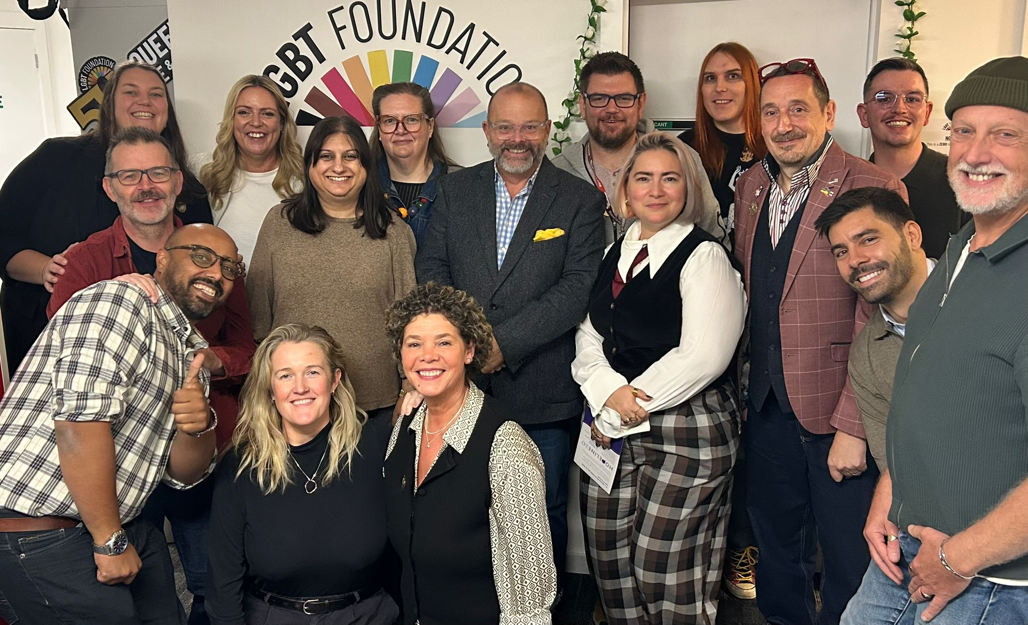 A group photo of our current trustees in our centre, with the LGBT Foundation logo in the background.