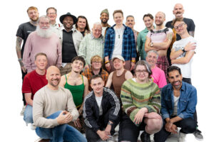 A large group of diverse LGBTQ+ men smiling and looking at the camera for LGBT Foundation's Man Enough campaign.