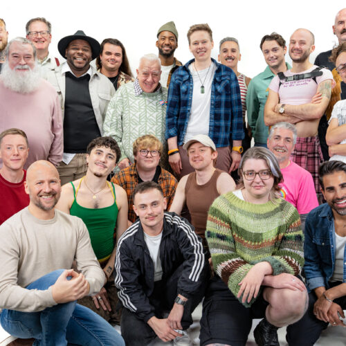 A large group of diverse LGBTQ+ men smiling and looking at the camera for LGBT Foundation's Man Enough campaign.