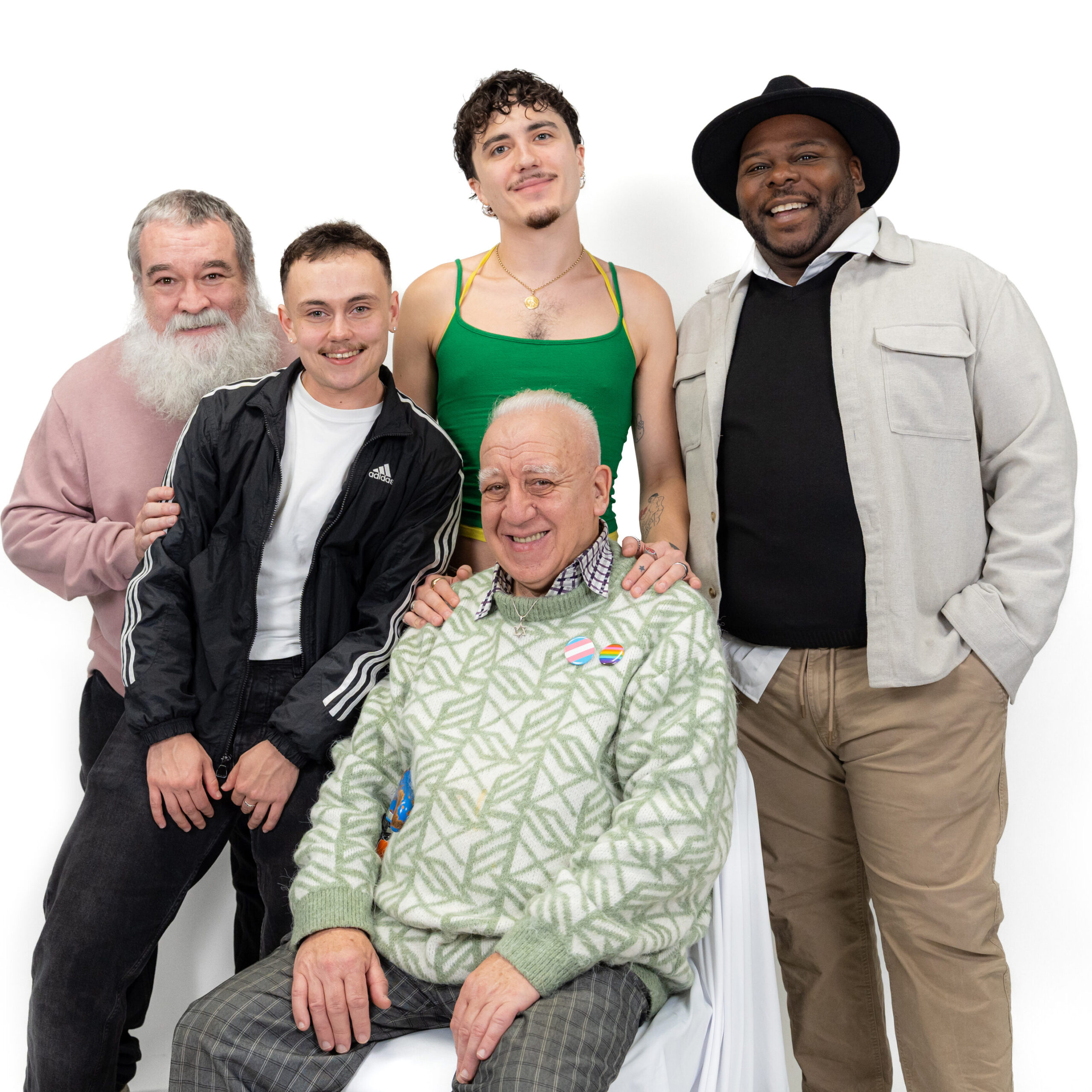 A group of LGBTQ+ men smiling and looking at the camera against a white backdrop for LGBT Foundation's Man Enough campaign