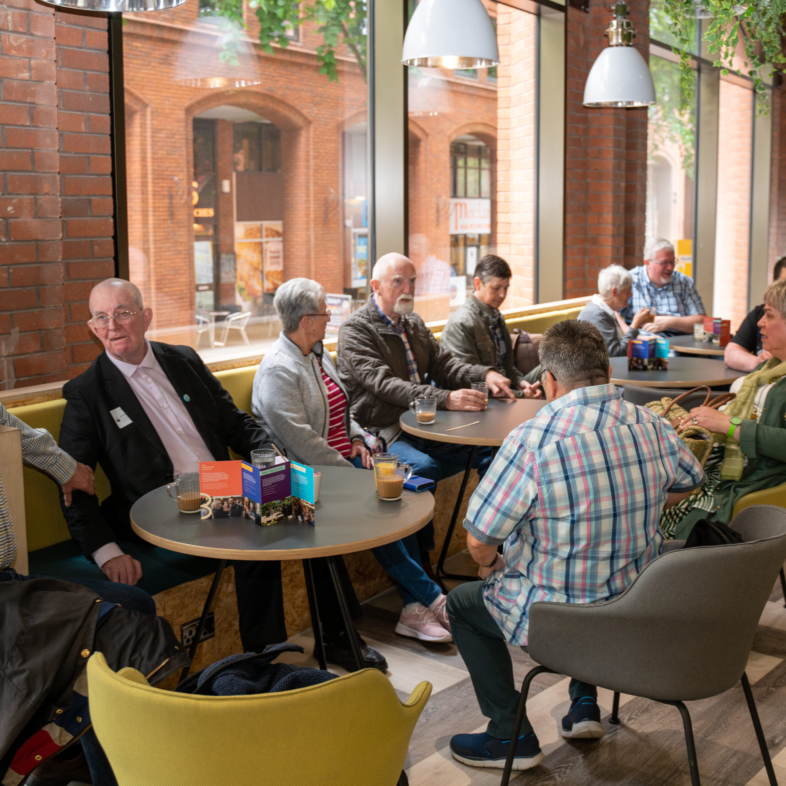 A wide shot of a group of older LGBTQ+ people in a café socialising