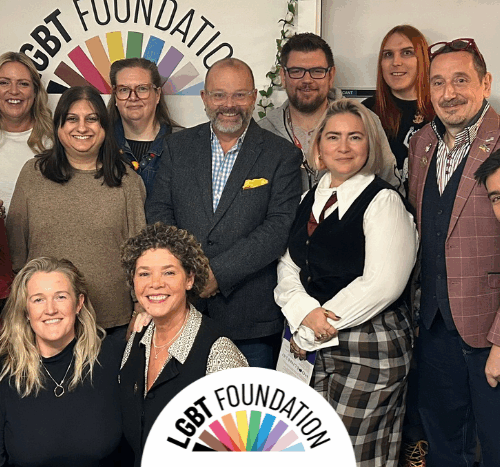 A group photo of our current trustees in our centre, with the LGBT Foundation logo in the background.