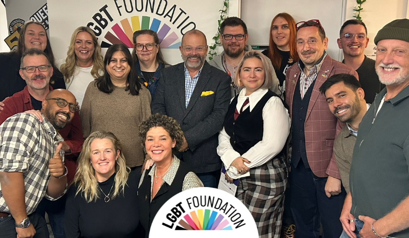 A group photo of our current trustees in our centre, with the LGBT Foundation logo in the background.