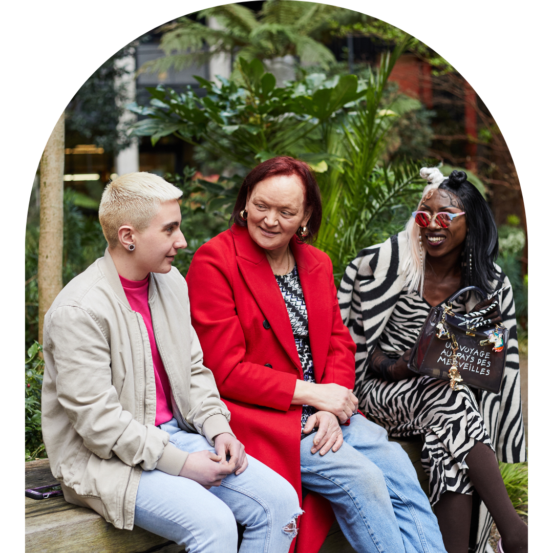 Arch frame photo of three LGBTQ+ people sitting outside and talking to each other.