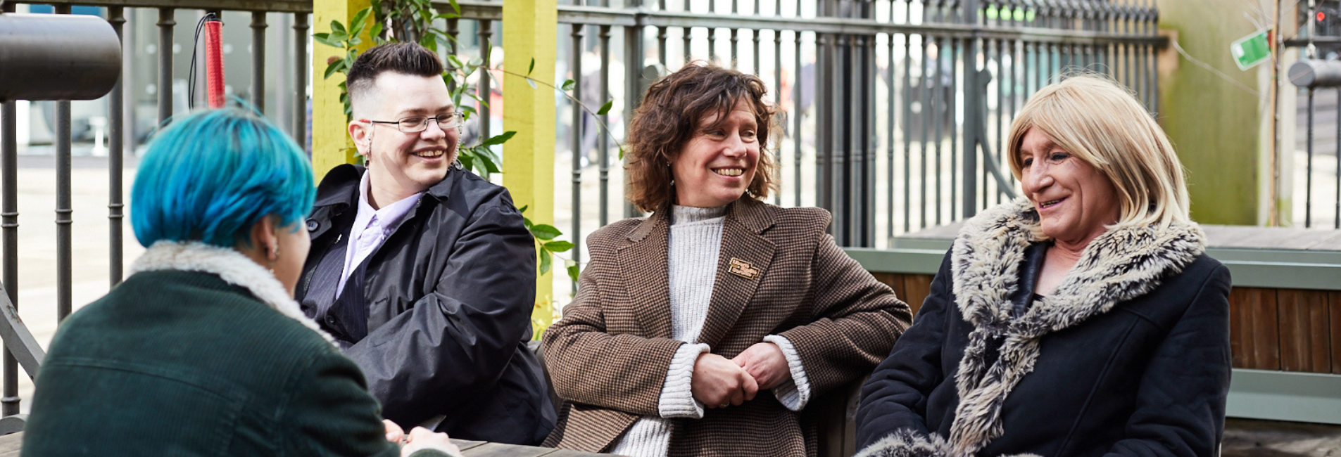 A group of four LGBT people sat at an outdoor table, smiling.